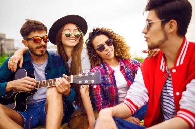 Grup arkadaşıyla birlikte eğleniyor. Adam gitar çalıyor. Herkes büyük bir ruh var.