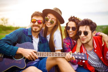 Grup arkadaşıyla birlikte eğleniyor. Adam gitar çalıyor. Herkes büyük bir ruh var.