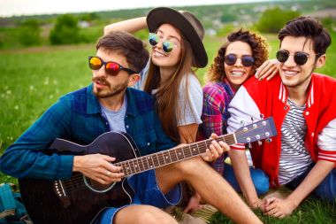 Grup arkadaşıyla birlikte eğleniyor. Adam gitar çalıyor. Herkes büyük bir ruh var.