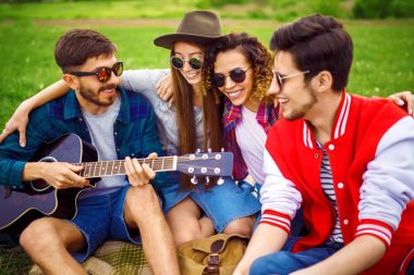 Grup arkadaşıyla birlikte eğleniyor. Adam gitar çalıyor. Herkes büyük bir ruh var.