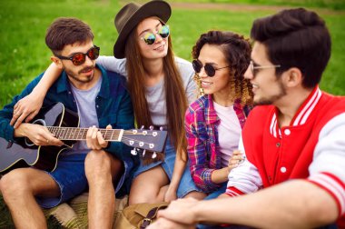 Grup arkadaşıyla birlikte eğleniyor. Adam gitar çalıyor. Herkes büyük bir ruh var.