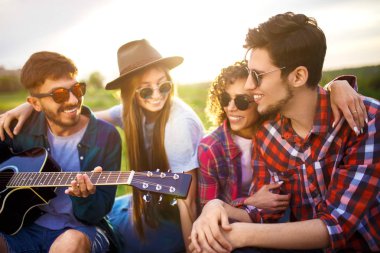 Grup arkadaşıyla birlikte eğleniyor. Adam gitar çalıyor. Herkes büyük bir ruh var.