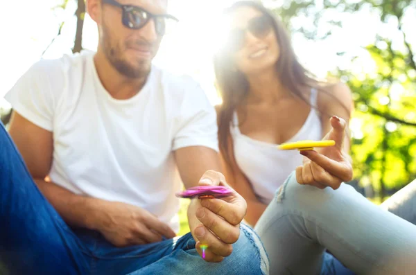 Jeune fille et garçon jouant avec un fidget spinners dans le parc. jouet anti-stress. Journée ensoleillée d'été. Ils rient et sourient — Photo