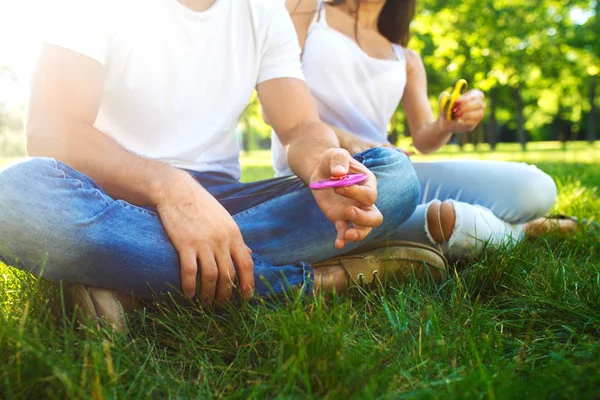 Fiatal lány és egy fiú játék-val egy izeg-mozog spinners a parkban. stressz enyhítésére játék. Napsütéses nyári napon. Nevetek, és mosoly — Stock Fotó