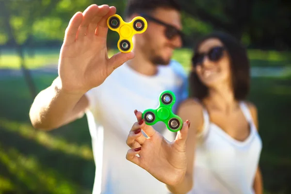 Jeune fille et garçon jouant avec un fidget spinners dans le parc. jouet anti-stress. Journée ensoleillée d'été. Ils rient et sourient — Photo