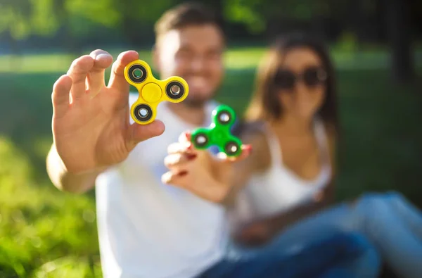 Jeune fille et garçon jouant avec un fidget spinners dans le parc. jouet anti-stress. Journée ensoleillée d'été. Ils rient et sourient — Photo