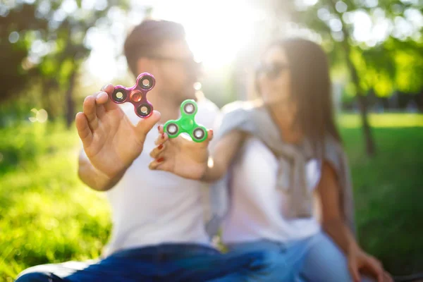 Jeune fille et garçon jouant avec un fidget spinners dans le parc. jouet anti-stress. Journée ensoleillée d'été. Ils rient et sourient — Photo