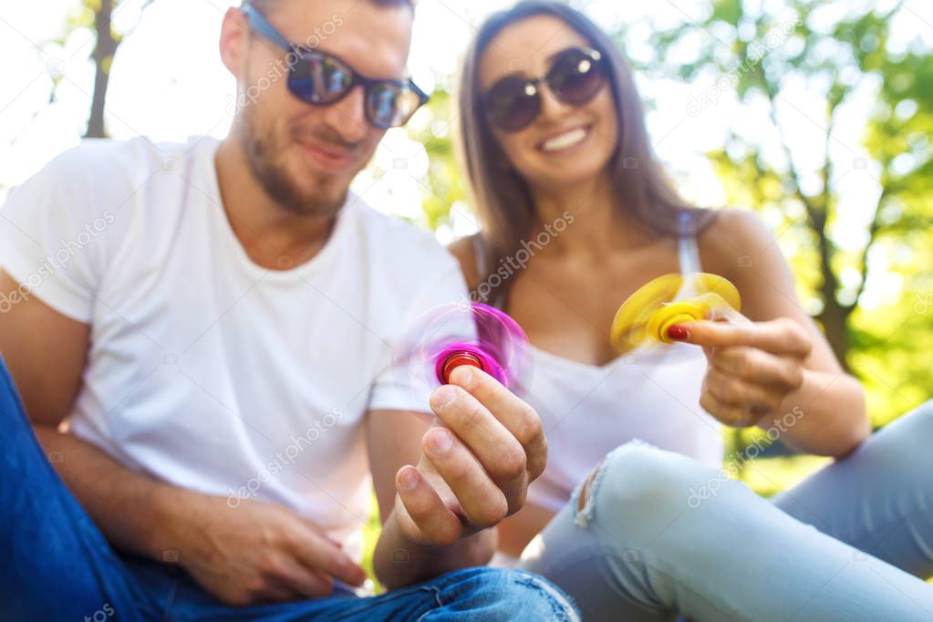 Young girl and boy playing with a fidget spinners in the park. stress relieving toy. Sunny summer day. They laugh and smile