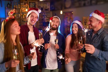 Havai fişekleri ile eğleniyor arkadaş grubu. Genç insanlar güler. Yeni yıl birlikte kutluyor. Grup Noel Baba şapkaları güzel genç insan. Arka plan bulanıklık