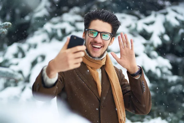 Close-up portrait of young beautiful men. Smiling young man having fun outdoors.the man is using the phone. A man loves winter. He is wearing a coat, a sweater and a scarf. Winter concept. Snowfall.