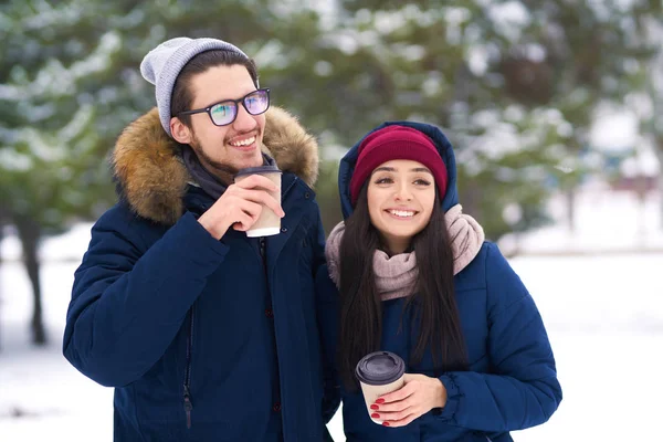 winter holidays, hot drinks and people concept - happy young couple with coffee in winter forest. people concept - happy couple in warm clothes outdoors.