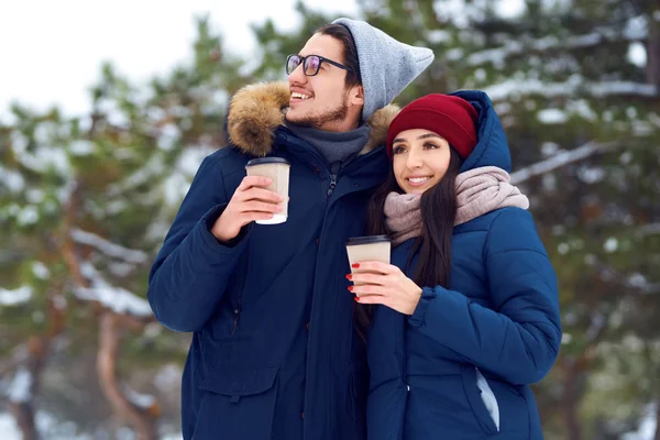 winter holidays, hot drinks and people concept - happy young couple with coffee in winter forest. people concept - happy couple in warm clothes outdoors.