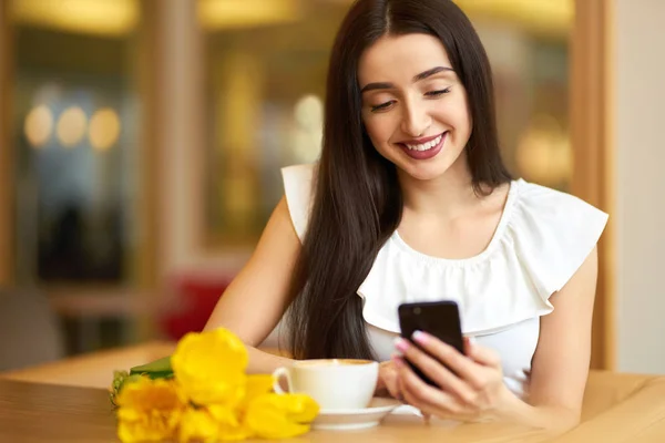 Beautiful Young Woman With Spring Tulips Flowers Bouquet At Cafe. Woman Drinking Coffee And Using Phone. Spring Style. Brunette Woman In Nice Spring.Beautiful Spring Mood. Fashion Spring/Summer.