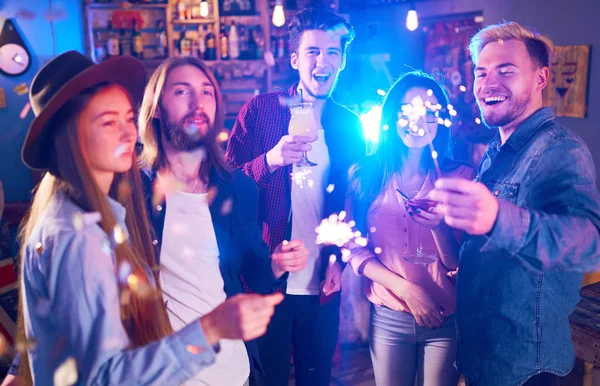 Young Group of Friends Partying In A Nightclub And Toasting Drinks. Happy Young People With Sparklers At Pub. The People Have A Great Mood And They Smile A Lot.