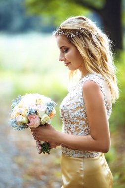 Bahçede yeşil çalılar arasında çarpıcı sarışın gelin standları.