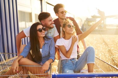 Selfie Zamanı! Grup alışveriş arabaları üzerinde eğleniyor mutlu genç insan. Alışveriş sepeti yarış çok ırklı çocuklar. Güzel yaz günü güneş ışığı ile. Yaşam tarzı kavramı 