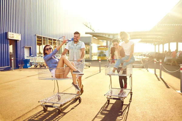 Group of happy young people having fun on shopping trolleys. Multiethnic young people racing on shopping cart. Beautiful summer day with sunlight. Lifestyle concept. Group of friends enjoy life.