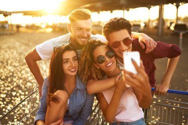 Selfie Zamanı! Grup alışveriş arabaları üzerinde eğleniyor mutlu genç insan. Alışveriş sepeti yarış çok ırklı çocuklar. Güzel yaz günü güneş ışığı ile. Yaşam tarzı kavramı 