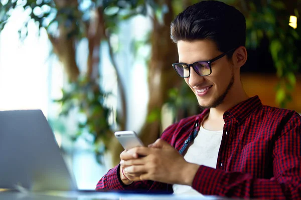 Masanın üstünde laptop ile gözlük gülümseyen genç hipster adam. Programcı, web geliştirici, mobil ve Masaüstü Web sürümleri karşılaştırarak ofiste çalışan tasarımcı.