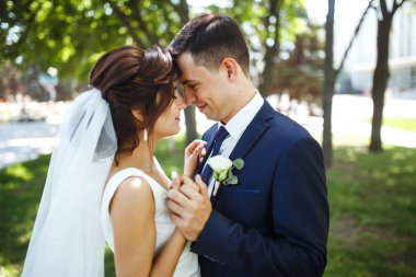 Gelin ve damat parkta birlikte yürürler. Beyaz elbiseli çekici gelin, damat koyu renkli şık bir takım elbise giyiyor. Güzel gelin ve şık damat. Düğün günü. Evlilik..