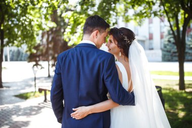 Gelin ve damat parkta birlikte yürürler. Beyaz elbiseli çekici gelin, damat koyu renkli şık bir takım elbise giyiyor. Güzel gelin ve şık damat. Düğün günü. Evlilik..
