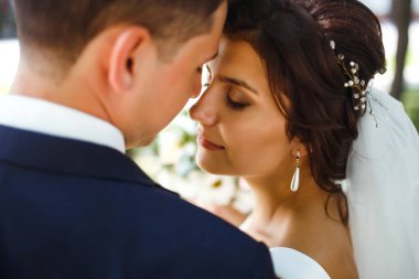 Gelin ve damat parkta birlikte yürürler. Beyaz elbiseli çekici gelin, damat koyu renkli şık bir takım elbise giyiyor. Güzel gelin ve şık damat. Düğün günü. Evlilik..