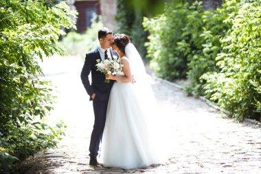 Gelin ve damat parkta birlikte yürürler. Beyaz elbiseli çekici gelin, damat koyu renkli şık bir takım elbise giyiyor. Güzel gelin ve şık damat. Düğün günü. Evlilik..