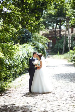 Gelin ve damat parkta birlikte yürürler. Beyaz elbiseli çekici gelin, damat koyu renkli şık bir takım elbise giyiyor. Güzel gelin ve şık damat. Düğün günü. Evlilik..