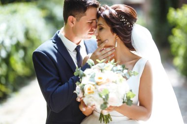 Gelin ve damat parkta birlikte yürürler. Beyaz elbiseli çekici gelin, damat koyu renkli şık bir takım elbise giyiyor. Güzel gelin ve şık damat. Düğün günü. Evlilik..