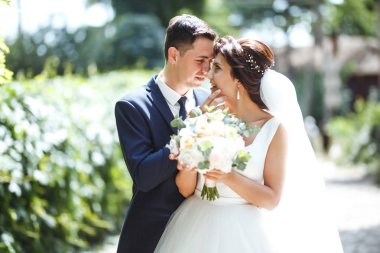 Gelin ve damat parkta birlikte yürürler. Beyaz elbiseli çekici gelin, damat koyu renkli şık bir takım elbise giyiyor. Güzel gelin ve şık damat. Düğün günü. Evlilik..