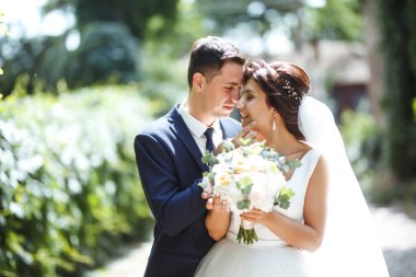 Gelin ve damat parkta birlikte yürürler. Beyaz elbiseli çekici gelin, damat koyu renkli şık bir takım elbise giyiyor. Güzel gelin ve şık damat. Düğün günü. Evlilik..