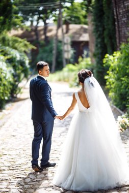 Gelin ve damat parkta birlikte yürürler. Beyaz elbiseli çekici gelin, damat koyu renkli şık bir takım elbise giyiyor. Güzel gelin ve şık damat. Düğün günü. Evlilik..