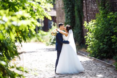 Gelin ve damat parkta birlikte yürürler. Beyaz elbiseli çekici gelin, damat koyu renkli şık bir takım elbise giyiyor. Güzel gelin ve şık damat. Düğün günü. Evlilik..