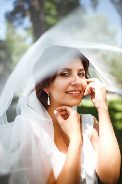 Duvağın altındaki gelinin güzel bir portresi. Profesyonel makyajlı ve saç stili olan zarif bir kadın. Bir duvağın altına gizlenmiş narin gelinlerin ellerinin fotoğrafı. Düğün günü. Evlilikten. Moda Gelini.