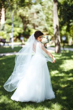 Parkta yürüyüş için bir buketi olan güzel bir gelin. Beyaz elbiseli genç gelin. Profesyonel makyajlı ve saç stili olan güzel bir kadın. Güzel bir gelin portresi. Düğün günü. Evlilik..