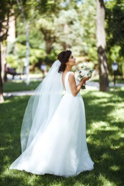 Parkta yürüyüş için bir buketi olan güzel bir gelin. Beyaz elbiseli genç gelin. Profesyonel makyajlı ve saç stili olan güzel bir kadın. Güzel bir gelin portresi. Düğün günü. Evlilik..