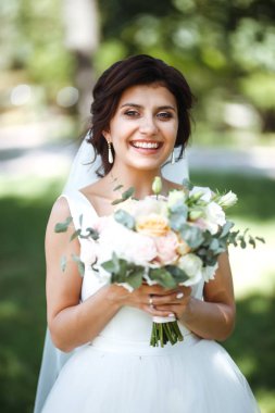 Parkta yürüyüş için bir buketi olan güzel bir gelin. Beyaz elbiseli genç gelin. Profesyonel makyajlı ve saç stili olan güzel bir kadın. Güzel bir gelin portresi. Düğün günü. Evlilik..
