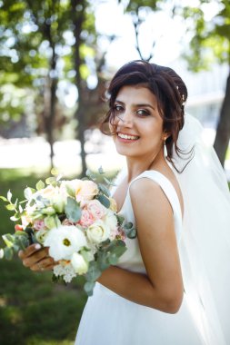 Parkta yürüyüş için bir buketi olan güzel bir gelin. Beyaz elbiseli genç gelin. Profesyonel makyajlı ve saç stili olan güzel bir kadın. Güzel bir gelin portresi. Düğün günü. Evlilik..