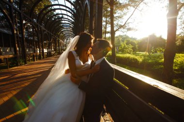 Gün batımında harika bir çift. Gelin ve damat bir buket çiçekle birlikte gün batımında yeşil tarlanın arka planına karşı ellerinde olacaklar. Romantik Evli Genç Aile. 