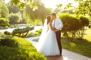 Gün batımında harika bir çift. Gelin ve damat bir buket çiçekle birlikte gün batımında yeşil tarlanın arka planına karşı ellerinde olacaklar. Romantik Evli Genç Aile. 