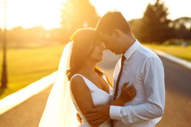 Gün batımında harika bir çift. Gelin ve damat bir buket çiçekle birlikte gün batımında yeşil tarlanın arka planına karşı ellerinde olacaklar. Romantik Evli Genç Aile. 