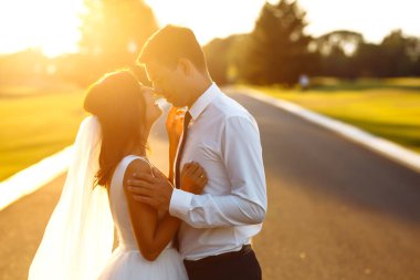 Gün batımında harika bir çift. Gelin ve damat bir buket çiçekle birlikte gün batımında yeşil tarlanın arka planına karşı ellerinde olacaklar. Romantik Evli Genç Aile. 
