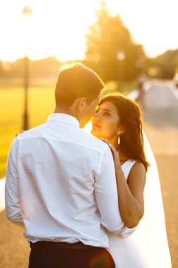 Gün batımında harika bir çift. Gelin ve damat bir buket çiçekle birlikte gün batımında yeşil tarlanın arka planına karşı ellerinde olacaklar. Romantik Evli Genç Aile. 