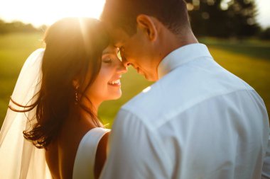 Gün batımında harika bir çift. Gelin ve damat bir buket çiçekle birlikte gün batımında yeşil tarlanın arka planına karşı ellerinde olacaklar. Romantik Evli Genç Aile. 