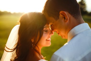 Gün batımında harika bir çift. Gelin ve damat bir buket çiçekle birlikte gün batımında yeşil tarlanın arka planına karşı ellerinde olacaklar. Romantik Evli Genç Aile. 