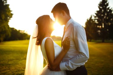 Gün batımında harika bir çift. Gelin ve damat bir buket çiçekle birlikte gün batımında yeşil tarlanın arka planına karşı ellerinde olacaklar. Romantik Evli Genç Aile. 