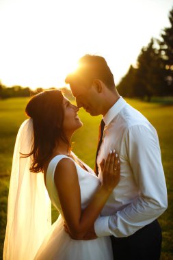 Gün batımında harika bir çift. Gelin ve damat bir buket çiçekle birlikte gün batımında yeşil tarlanın arka planına karşı ellerinde olacaklar. Romantik Evli Genç Aile. 