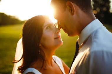 Gün batımında harika bir çift. Gelin ve damat bir buket çiçekle birlikte gün batımında yeşil tarlanın arka planına karşı ellerinde olacaklar. Romantik Evli Genç Aile. 