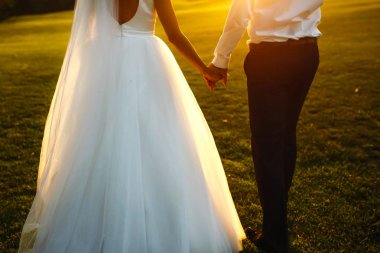 Gün batımında harika bir çift. Gelin ve damat bir buket çiçekle birlikte gün batımında yeşil tarlanın arka planına karşı ellerinde olacaklar. Romantik Evli Genç Aile. 