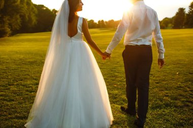 Gün batımında harika bir çift. Gelin ve damat bir buket çiçekle birlikte gün batımında yeşil tarlanın arka planına karşı ellerinde olacaklar. Romantik Evli Genç Aile. 